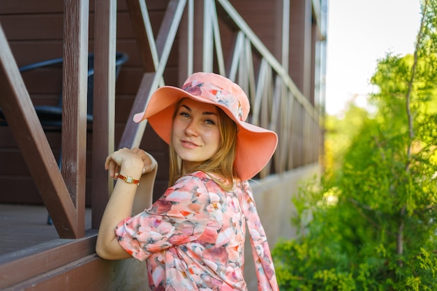 明るい夏のサンドレスとパレオの帽子をかぶった魅力的な女の子が緑豊かな公園を歩いています。