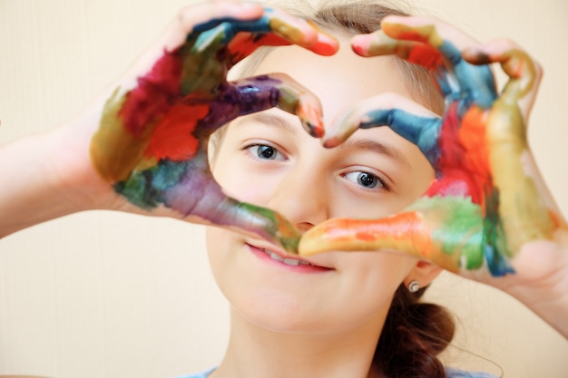 Foto affascinante ragazza che guarda la telecamera attraverso il cuore facendo gesti con le mani in vernici colorate