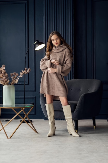 Charming girl with hair in posing in her mothers suede boots Childhood young actress glamor Full length shot isolated interior background Girl 79 years old hands at the face