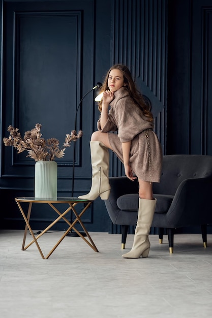 Charming girl with hair in posing in her mothers suede boots Childhood young actress glamor Full length shot isolated interior background Girl 79 years old hands at the face