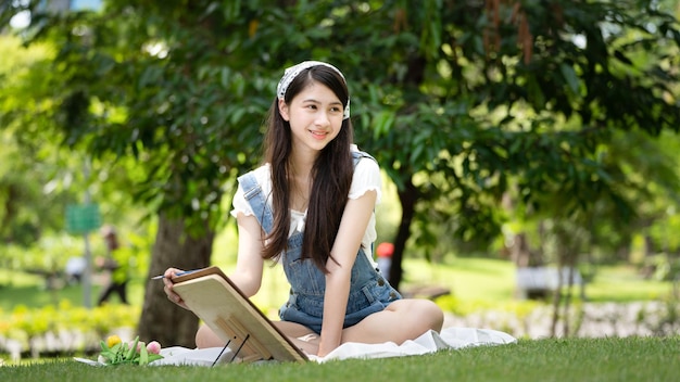 Charming Girl woman sitting on plaid at the park in sunny summer day and using watercolor