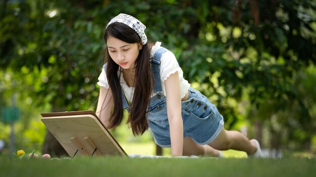 화창한 여름날 공원에서 격자 무늬에 앉아 수채화를 사용하는 매력적인 소녀 여성