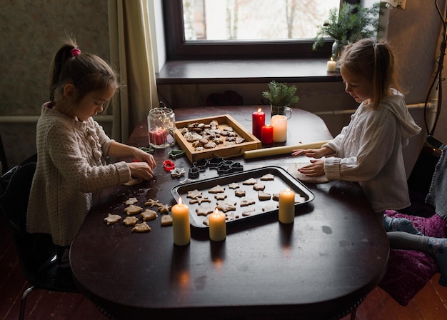 Charming girls cook Christmas cookies together at home at the table