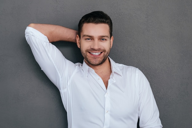 Charming handsome. Handsome young man holding hand behind head and smiling