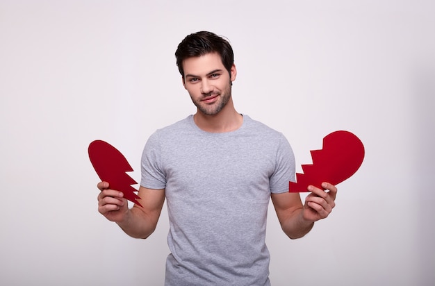 Uomo bello affascinante con un cuore rotto rosso su un bianco.