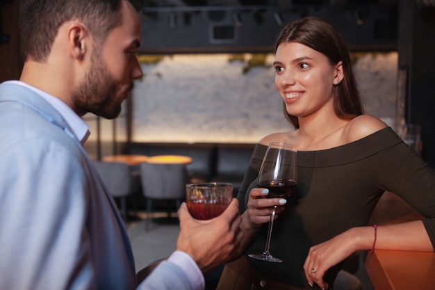Очаровательная счастливая молодая женщина пьет коктейли со своим парнем в баре