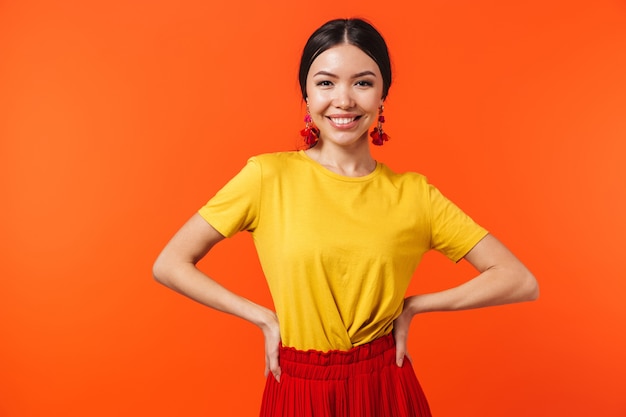 charming hispanic woman 20s dressed in skirt laughing at camera isolated over red wall