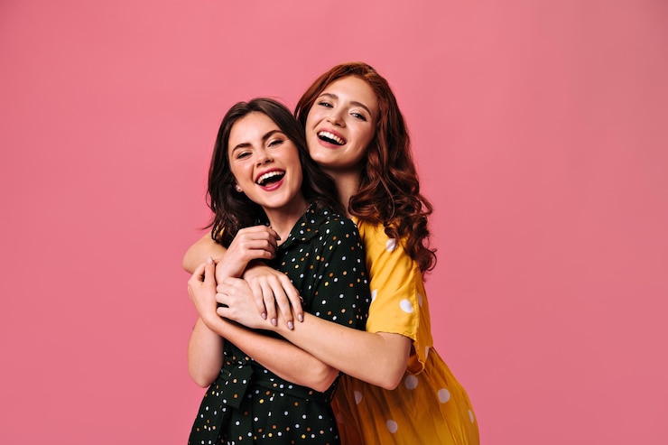 Photo charming ladies look into camera and hug fashionable women in great polka dot dresses have fun together and embrace