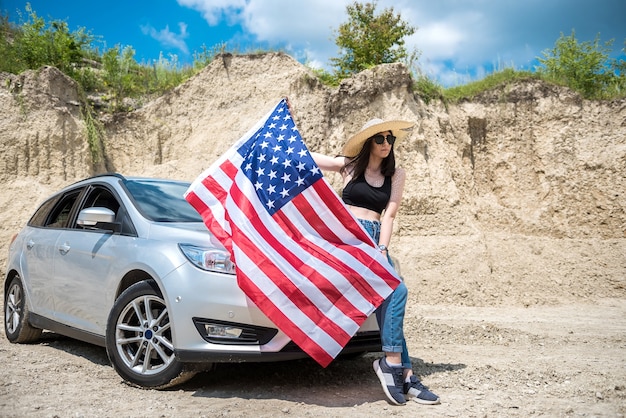 Charming lady with the USA flag near the car in a sand quarry in summer