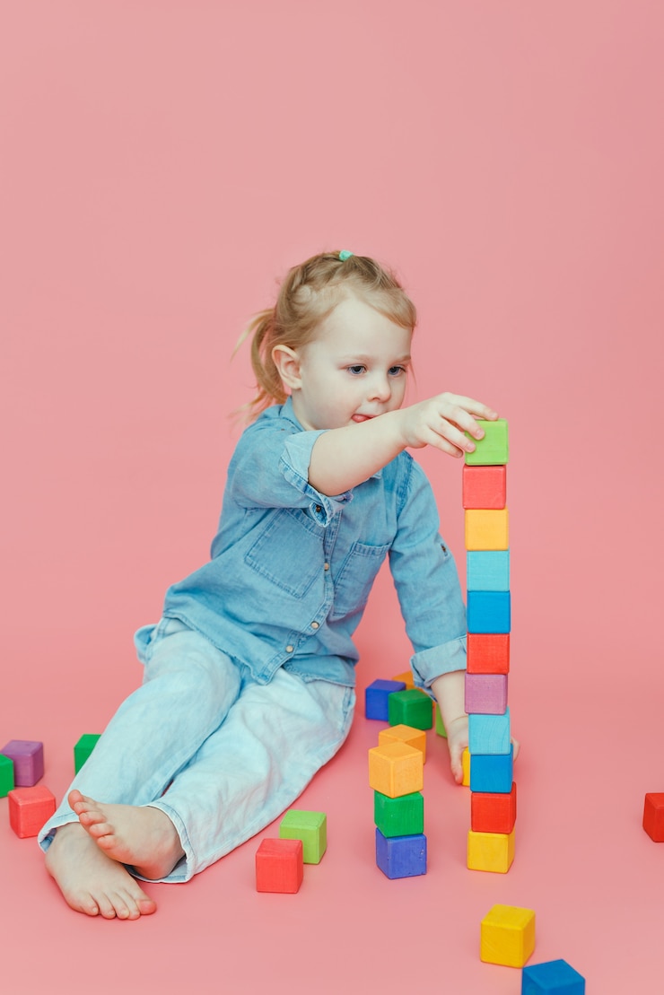 魅力的な小さな女の子が木の色の立方体の塔を建てます。