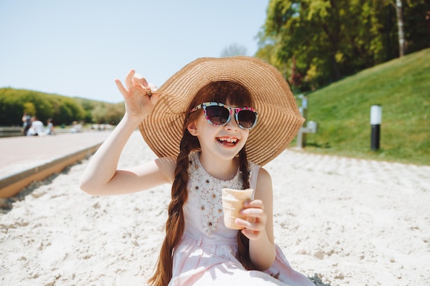 Charming little girl in a hat eats ice cream on the beach of the beach Summer vacation concept