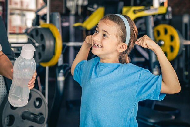 Charming little girl is shows her biceps working out at gym