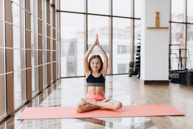 Charming little girl is smiling while doing yoga in fitness hall