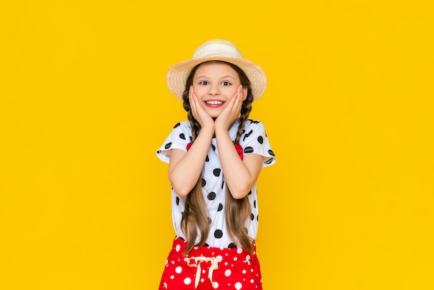 Un'affascinante bambina con un cappello di paglia un bel bambino si rallegra in estate e tiene le guance con le mani carina ragazza adolescente su uno sfondo giallo isolato