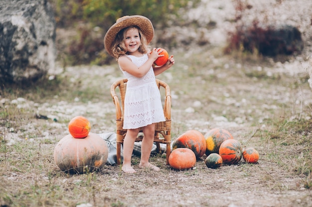 charming little girl in a straw hat, wicker chair, pumpkins, autumn