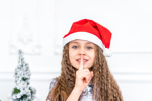 Charming little girl wearing a Santa hat smiles next to Christmas decorations