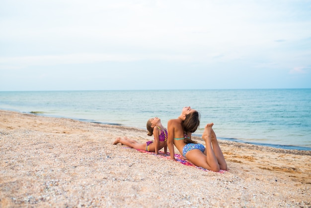 Charming little girls do gymnastic exercises while relaxing on the beach on a sunny warm summer day. The concept of sports and active games in the summer. Copyspace