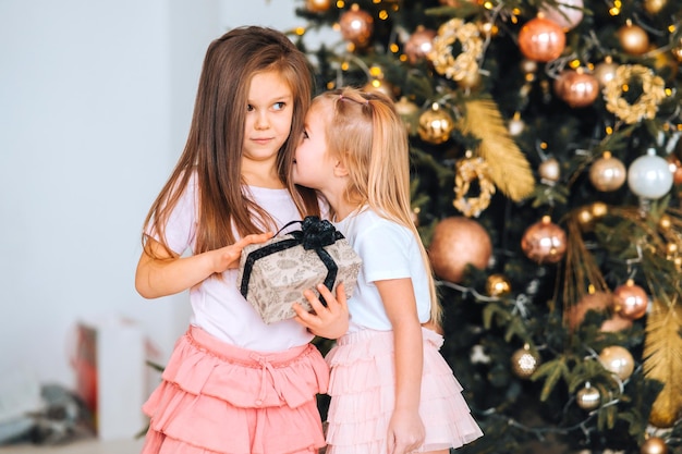 Charming little girls holds a gift on a background of christmas trees