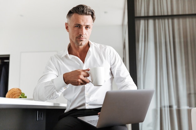 Charming man dressed in formal clothes using laptop