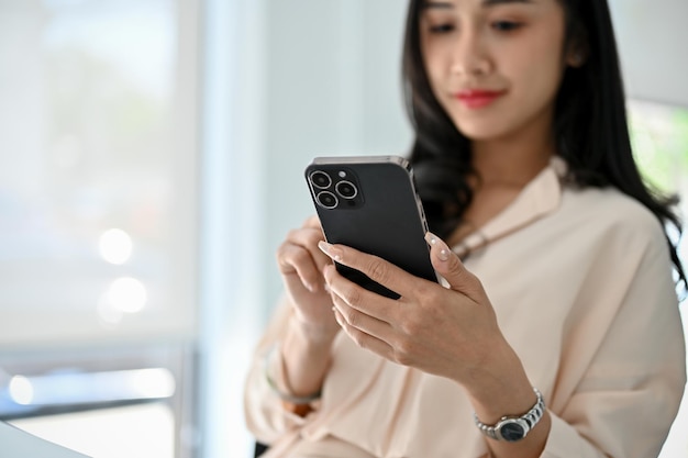 Charming millennial Asian businesswoman using her smartphone at her desk selective focus