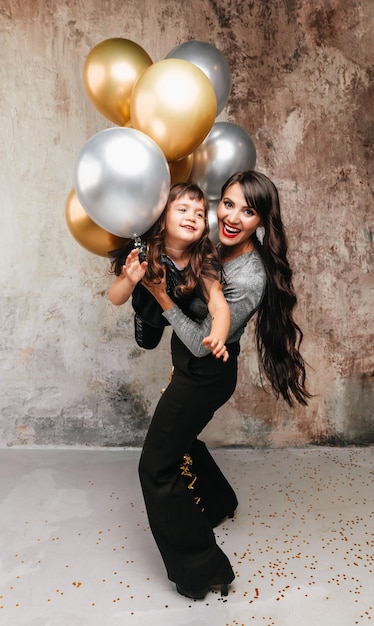 Charming mom and little daughter in the same outfit pose together after a birthday party Portrait of a charming girl hugging her daughter balloons