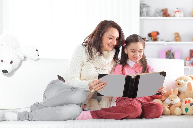 Charming mother and daughter reading a book sitting on the couchphoto with copy space