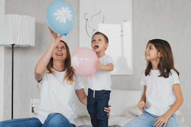 Charming mother and her children daughter and little son have fun at home on the bed