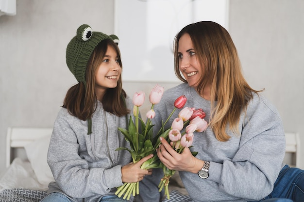 Charming mother with a bouquet of tulips and her daughter have fun at home