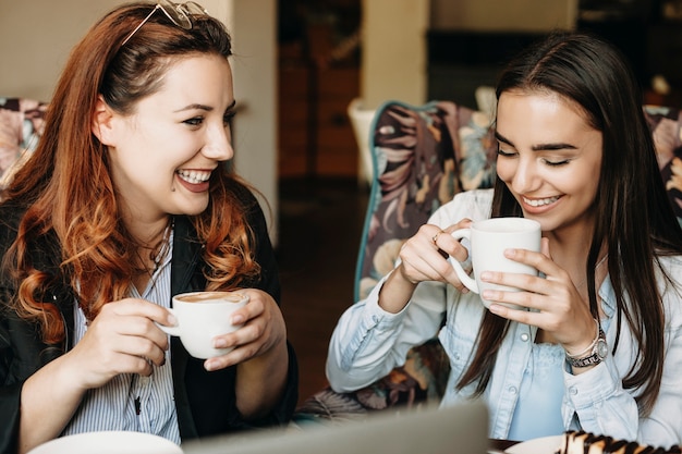 コーヒーを飲み、カフェで彼女の素敵な女性の友人と笑顔の赤い髪の魅力的なプラスサイズの女性。