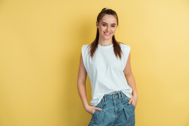 Charming, positive girl in a white Tshirt stands on the background of an yellow wall.