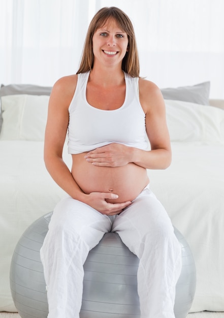 Charming pregnant female caressing her belly while sitting on a gym ball