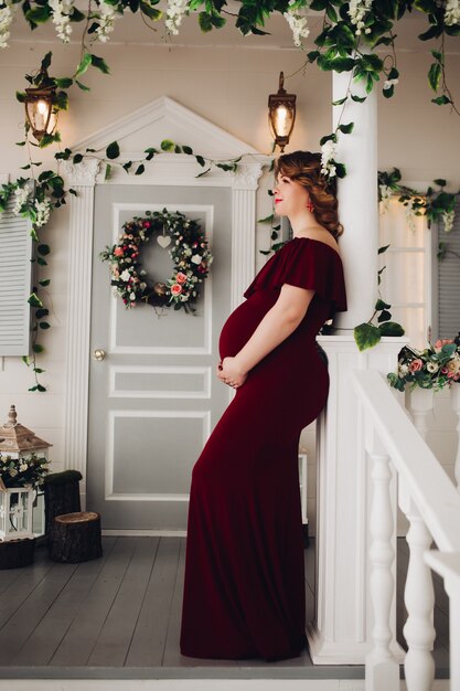 Charming pregnant woman in marsala dress posing on steps of house