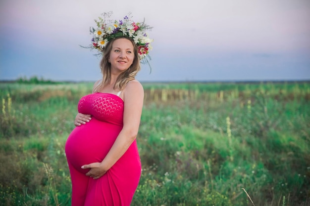 charming pregnant woman with a wreath in the field