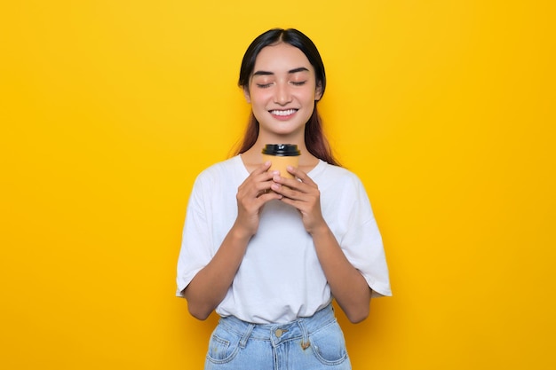 Charming pretty young girl in white tshirt holding coffee cup isolated on yellow background