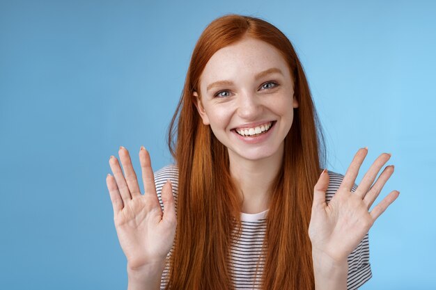 魅力的な赤毛の姉は、さようなら兄弟の友人が陽気な手を振って上げられた手のひらを笑って、10本の指がうれしそうにニヤリと笑ってのんびりとリラックスして、何気なく青い背景を話していることを示しています。