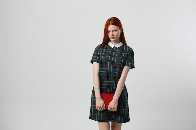 charming redhead long-haired girl in a green checkered dress walks with books in her hands