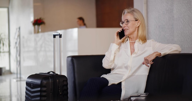 Charming senior woman talking on mobile phone in hotel waiting area