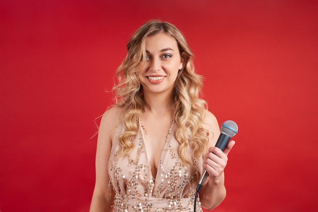 Charming singer in a beautiful dress with a microphone posing on a red background