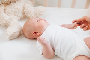 A charming smiling blueeyed 2monthold baby in a white bodysuit lies in a crib next to a teddy bear view from above a newborn