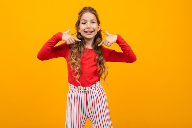 Charming teenager girl in a red blouse and striped trousers shows emotions on yellow with copy space