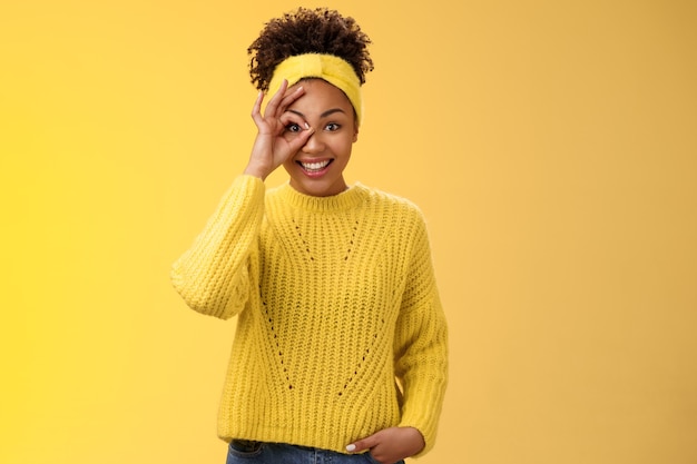 Charming tender feminine african-american girlfriend show circle on eye ok okay gesture look lucky happily smiling satisfied impressed waiting excitement travel friends, yellow background.