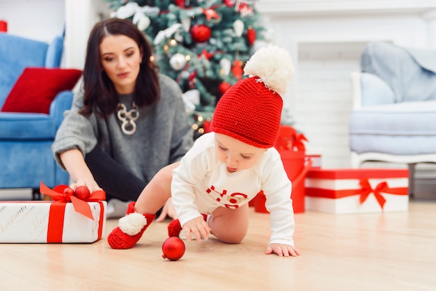 Charming toddler with her mother unpacking holidays gift.