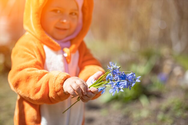 日光の下で屋外の春の花を持つ魅力的な幼児