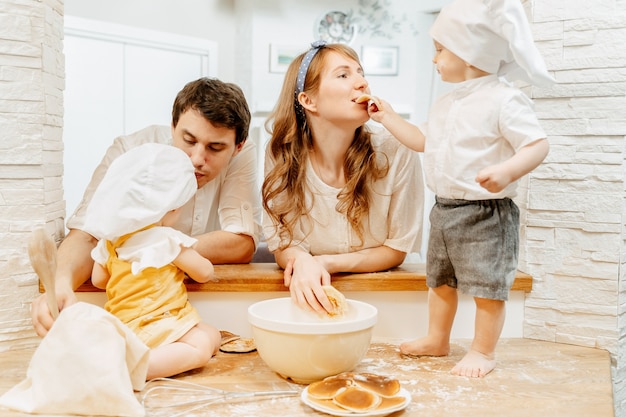 L'affascinante bambino di due anni fa provare a sua madre a cuocere i pancake durante la cucina di famiglia con papà e sorella. concetto di hobby ed esperienze di sviluppo congiunto con i bambini