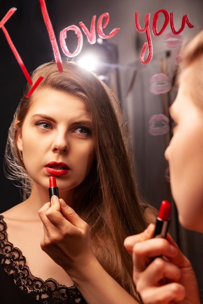 Charming woman applying red lipstick and looking in mirror