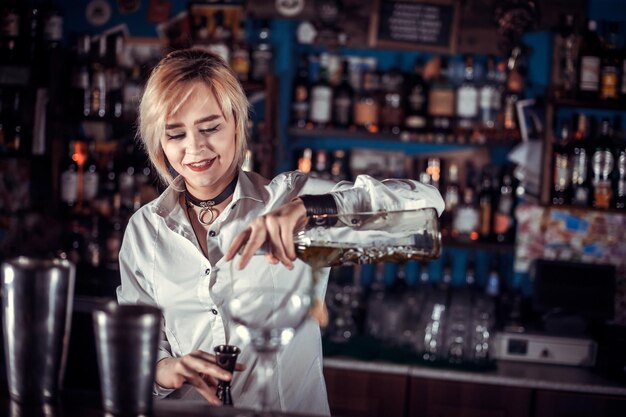 Charming woman bartending formulates a cocktail while standing near the bar counter in pub