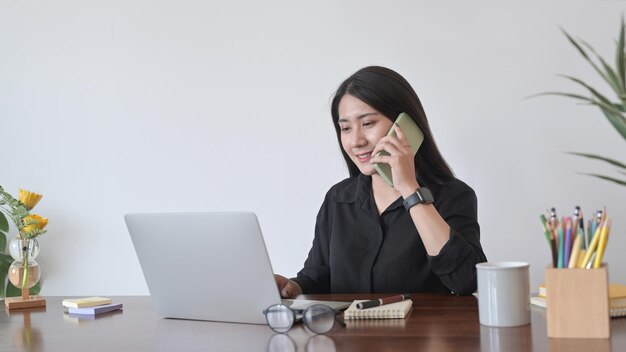 Charming woman having conversation with mobile phone and using laptop in cafe