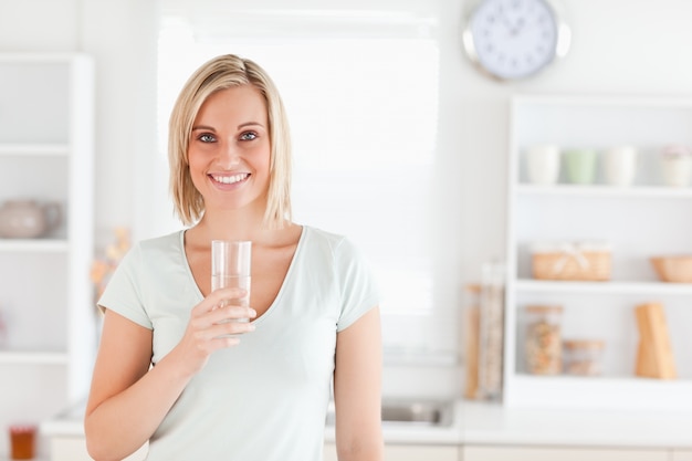 Charming woman holding glass filled with water while standing looking into the camera