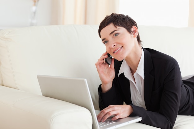 Charming Woman lying on a sofa with a laptop and a phone