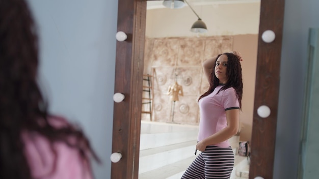 Charming woman in pajama looking in mirror Side view of young lady in purple pajama smiling while looking over shoulder in mirror in modern bedroom